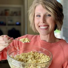 a woman holding a bowl of cereal and spoon in front of her face, smiling at the camera