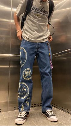 a man standing in front of an elevator with his back to the camera, wearing jeans and a backpack