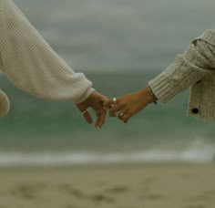 two people holding hands on the beach with waves in the backgroung behind them