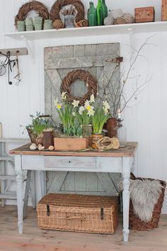 a white table with flowers and baskets on it's shelf next to a wall