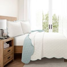 a bed with white sheets and pillows in a room next to a window, near a dresser