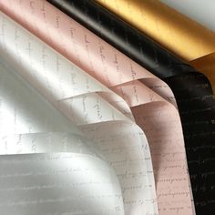 four different colored papers are lined up on a tablecloth with gold, black, and white writing