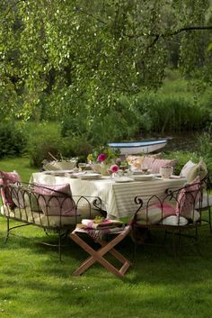 an outdoor table set up with pink and white linens in the middle of a grassy area