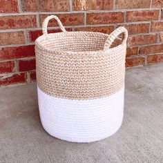 a large white and beige basket sitting on the ground next to a brick wall,