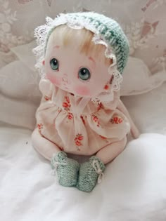 a small doll sitting on top of a white bed next to a lace doily