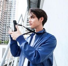 a young man holding a camera up to his face while standing next to a building