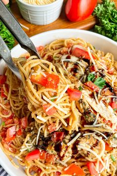 someone is cutting up some spaghetti with tomatoes and basil on top, in a white bowl