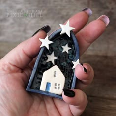 a hand holding a miniature house with stars on it