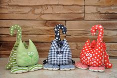 three colorful stuffed animals sitting next to each other on top of a wooden floor in front of a stone wall