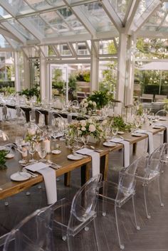 a long table is set with clear chairs and place settings for dinner guests to sit at