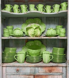 a green china cabinet filled with lots of green plates and cups on top of wooden shelves