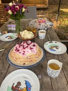 a table topped with plates and cake on top of a wooden table next to flowers