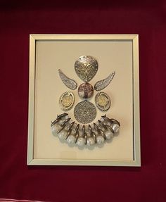 an art piece with silver and pearls on display in a white framed frame against a red background