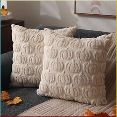 two decorative pillows sitting on top of a couch in front of a wall with autumn leaves