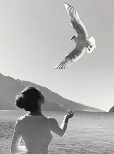 a woman is looking at a bird flying over the water