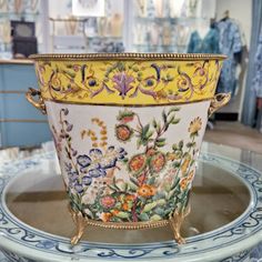 a yellow and blue flower pot sitting on top of a glass table in a store