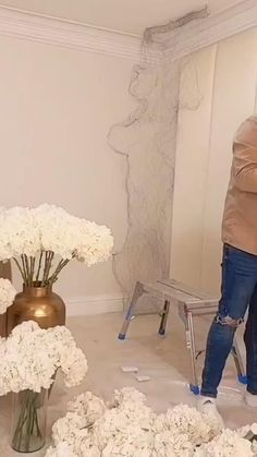 a man that is standing in front of a bunch of flowers on the wall with his feet up