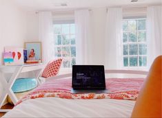 a laptop computer sitting on top of a bed in a room with white walls and windows