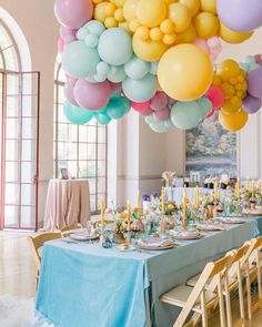 a table set up for a party with balloons and flowers on the ceiling above it