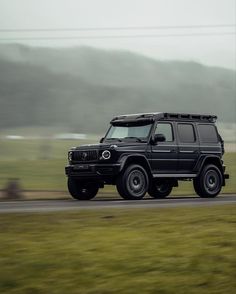 a black jeep driving down a road next to a green grass covered field and hills