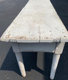 an old white wooden table sitting on top of a parking lot with no one around it