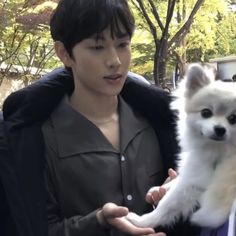 a man holding a small white dog in his hands while standing next to another person