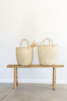 two baskets sitting on top of a wooden bench next to each other in front of a white wall