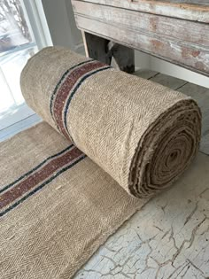 two rolled up rugs sitting on the floor in front of a wooden bench and window