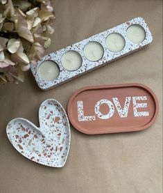 three candles in trays with the word love painted on them next to some flowers