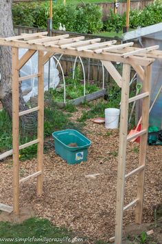 a wooden structure in the middle of a garden with a green bucket and shovels