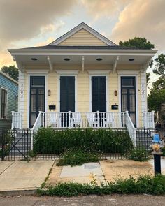 a small yellow house with black shutters on the front porch and white picket fence