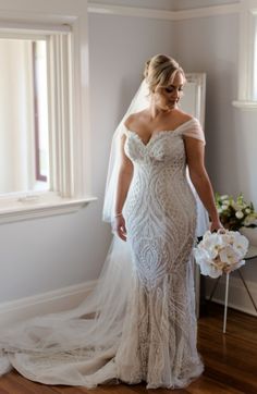 a woman in a wedding dress standing next to a window