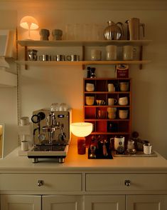 an espresso machine sitting on top of a counter next to a shelf filled with cups