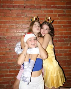 three girls in costumes hugging each other near a brick wall