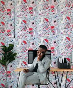 a man sitting at a desk talking on a cell phone in front of a colorful wallpaper