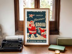 an old fashioned christmas poster next to a typewriter on a wooden desk in front of a window