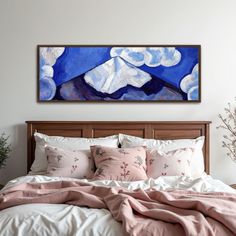 a bed with pillows and blankets on top of it in front of a large painting