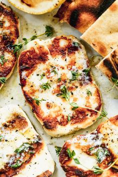 several slices of pizza with cheese and herbs on them sitting on a table next to pita bread