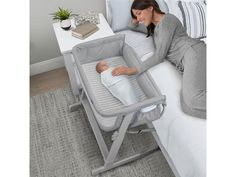 a woman laying in bed next to a baby's bassinet and changing table