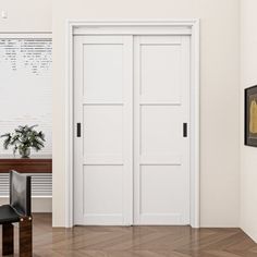 an empty room with two white doors and a black chair in the corner, next to a wooden table