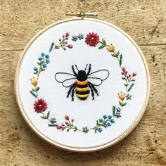 a cross stitch bee sitting on top of a wooden table next to a flower wreath