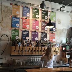 a woman standing in front of a bar filled with lots of bottles and glasses on the wall