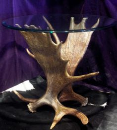 a glass and wood table with antlers on the top, sitting in front of a purple curtain