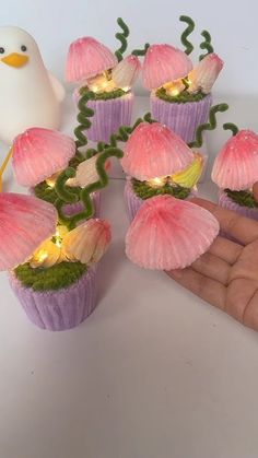 a hand is holding some cupcakes with pink flowers on them and lights in the middle