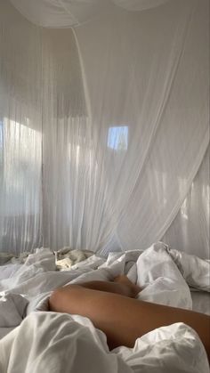 a woman laying in bed covered with white sheets