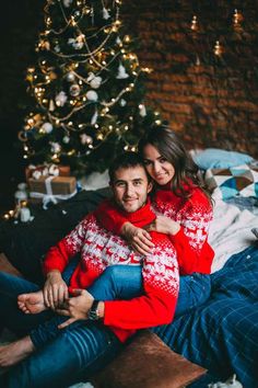 a man and woman sitting next to a christmas tree