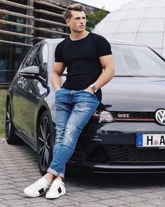 a man sitting on the hood of a black car with his hands in his pockets