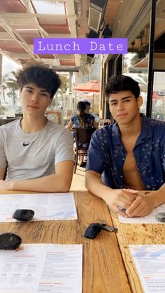 two young men sitting at a table with paper on it