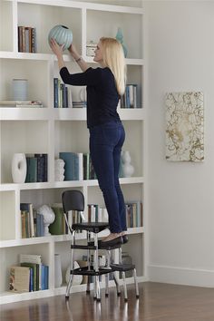 a woman is standing on a chair and holding a ball in the air above her head