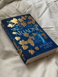 a blue book sitting on top of a white bed covered in sheets and pillows with gold leaves